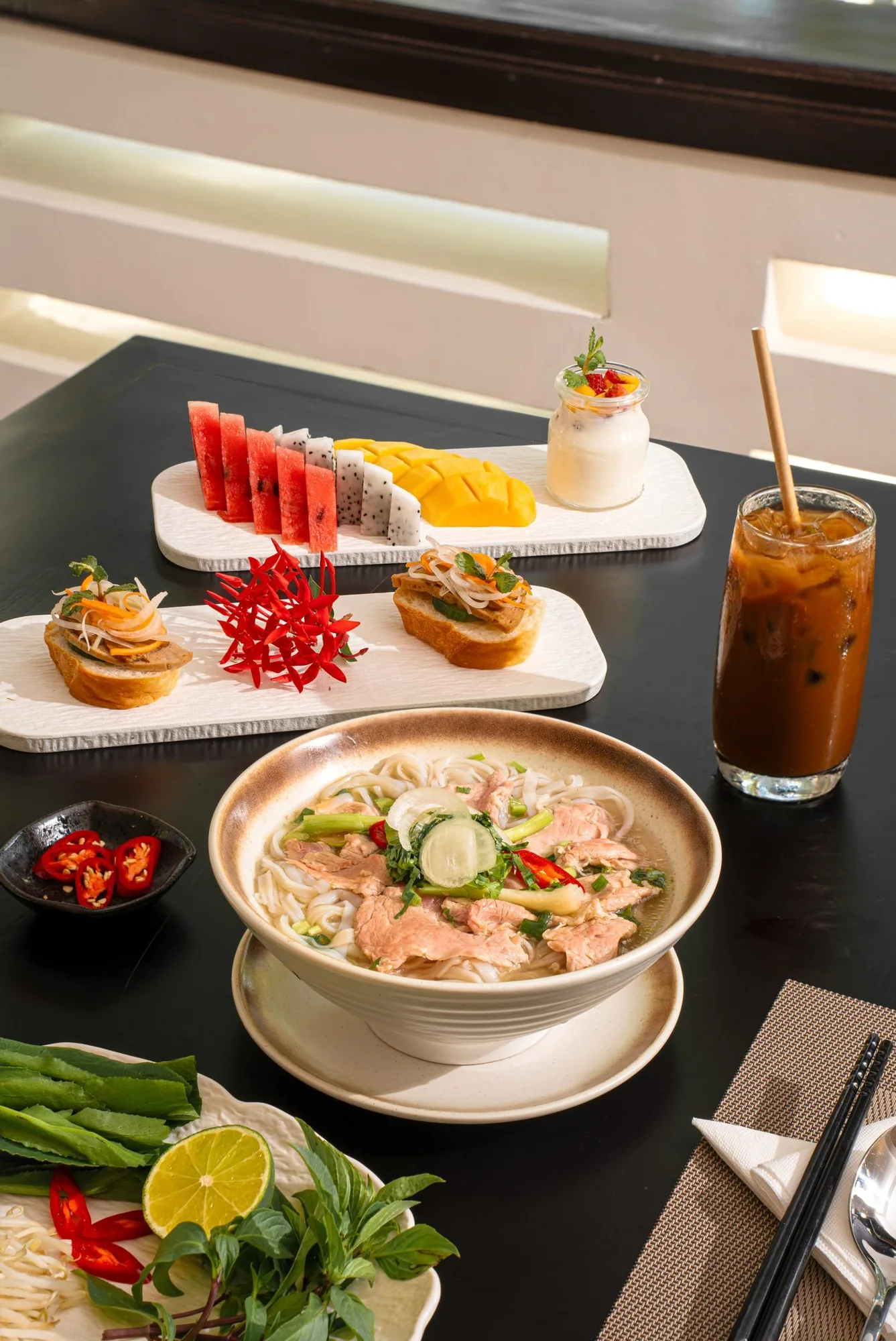Vietnamese breakfast at Faifo: a bowl of pho with herbs and lime, small plates and Vietnamese iced coffee