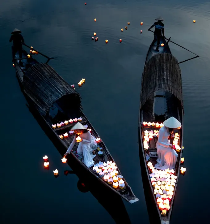 Two wooden boats on the river at dusk, loaded with paper lanterns being set on the water