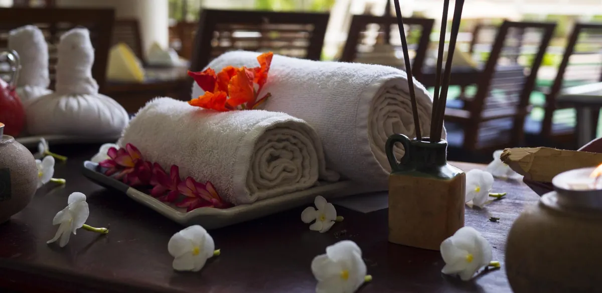 Two rolled white towels with red and white flowers and a reed diffuser on a spa table