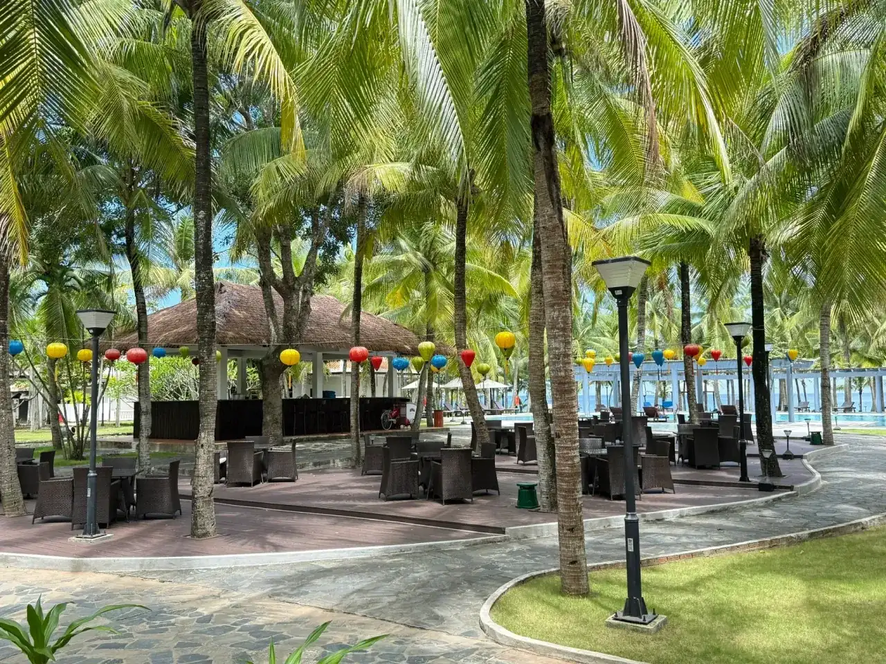 The Pool Bar: a thatched bar, silk lanterns and a rattan terrace under the palms, with the pool behind