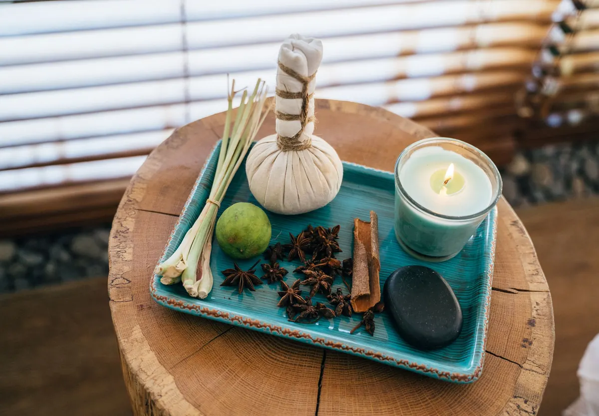 A herbal compress on a turquoise tray with lemongrass, lime, star anise, cinnamon, a stone and a candle