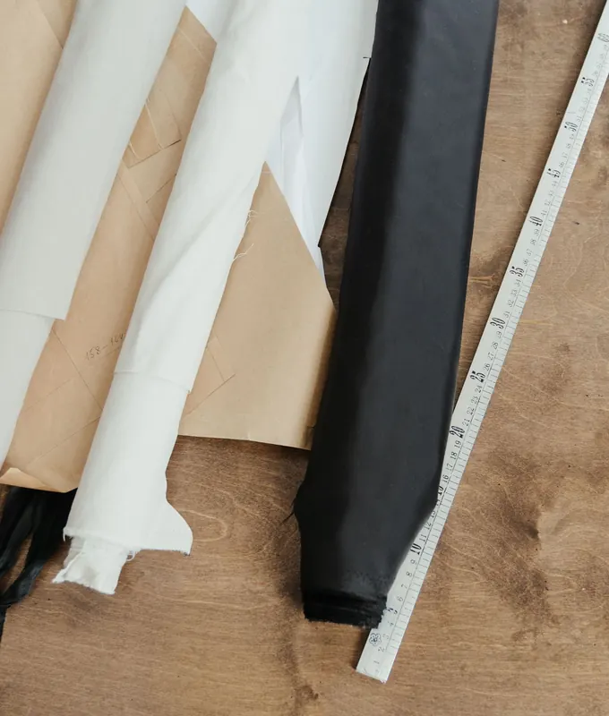 Rolls of white and black fabric, pattern paper and a tape measure on a tailor’s table