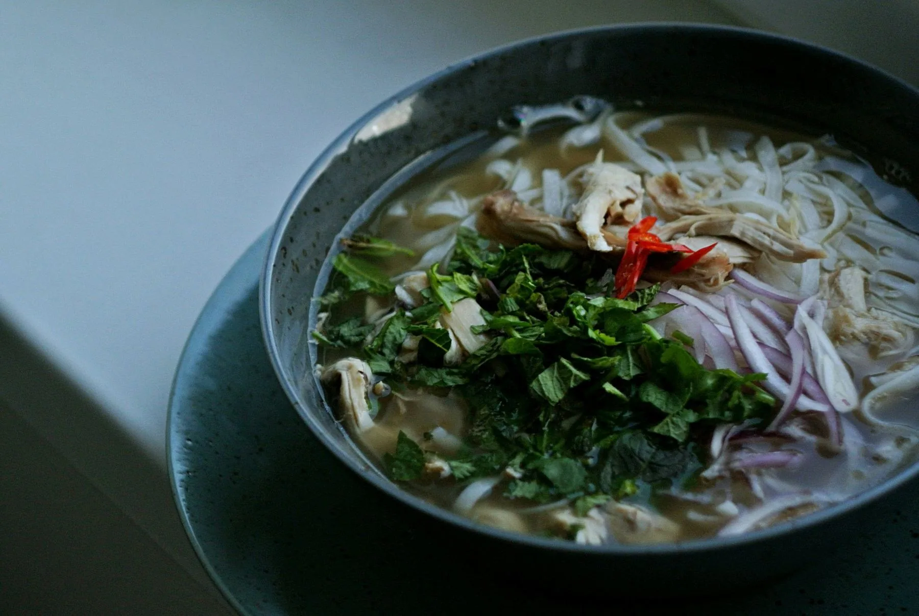 A bowl of pho with rice noodle, herbs and chilli