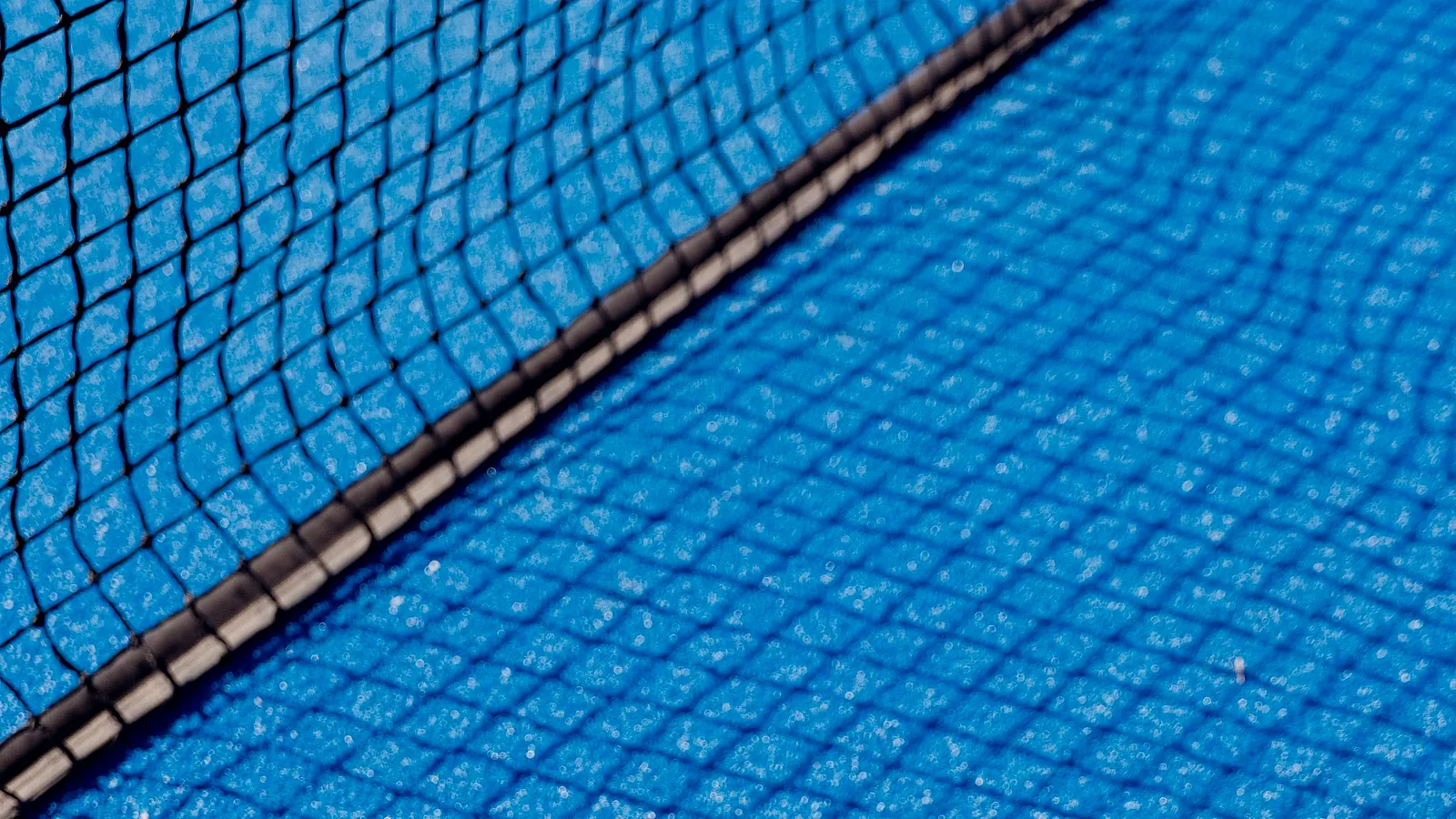 A court net and its shadow on bright blue artificial turf, in full sun