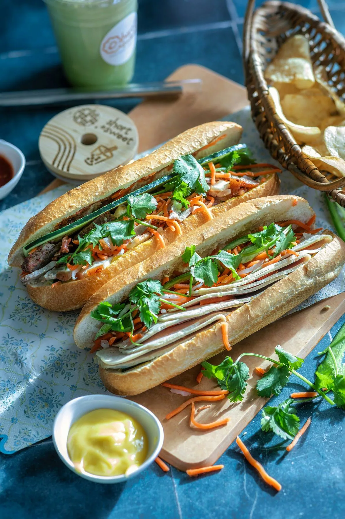 Three banh mi with herbs and pickled vegetables on a blue table