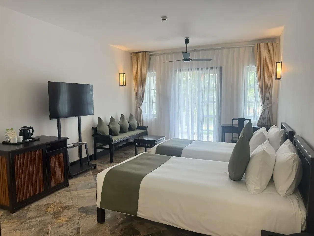 La Standard Room desde la entrada: minibar, televisión, un banco con cojines verde oliva, el ventanal y las dos camas twin